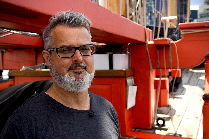James Hunter, with mustache, beard and thin-rimmed black glasses, smiles. In the background is red industrial machinery.