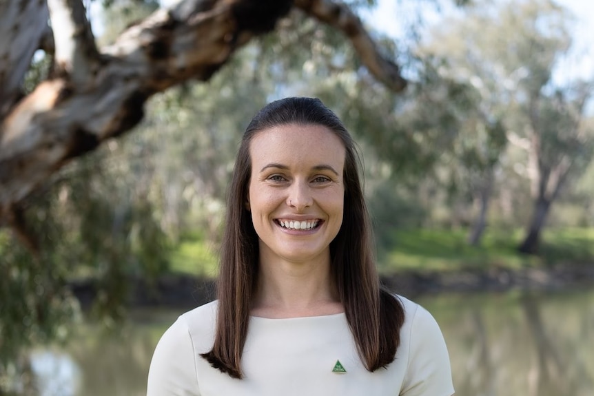 A woman stands next to a tree and smiles at camera