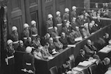 A black-and-white wartime photo of a court room with people seated and soldiers around.