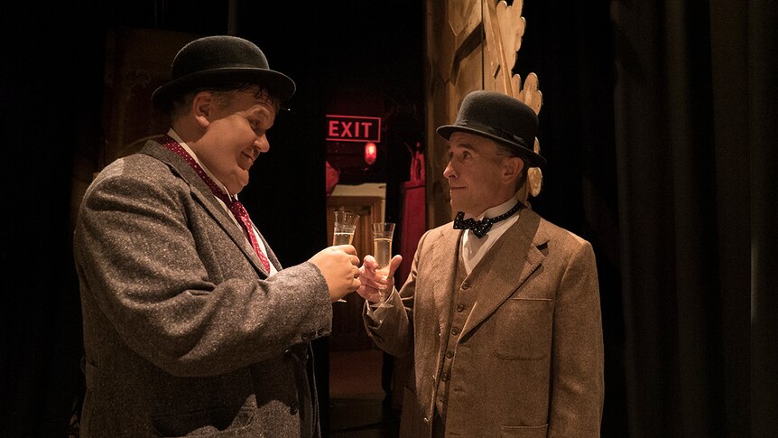 Colour still of Steve Coogan and John C. Reilly clinking glasses backstage in 2018 film Stan and Ollie.