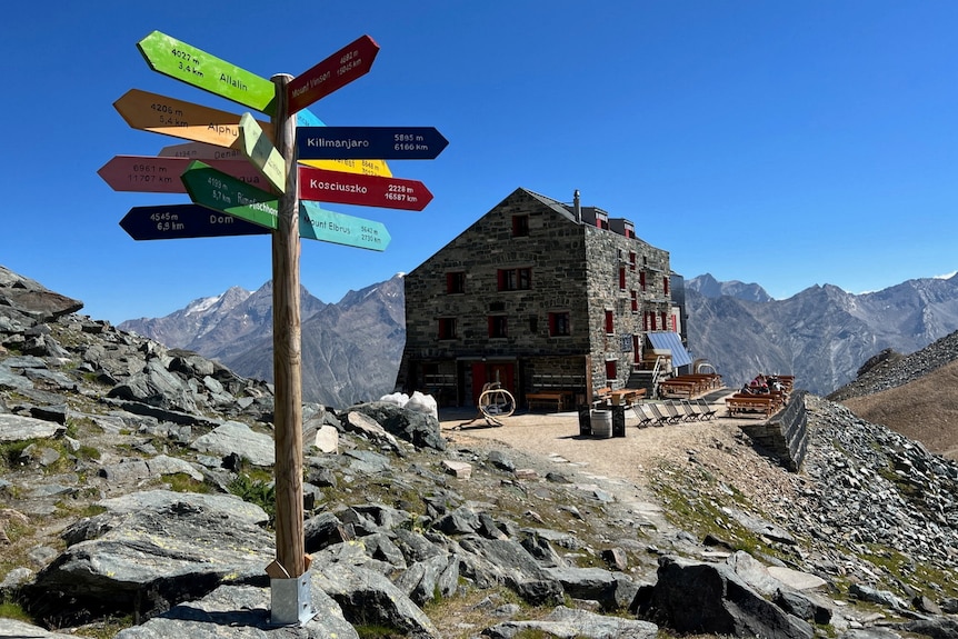 A signpost and a hut on the side of a mountain. 