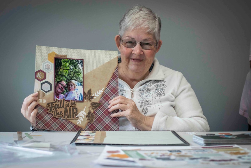 A woman with silver hair holds up a scrapbook
