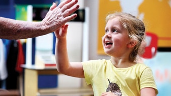Smiling young girl high fives with an elderly woman off camera.