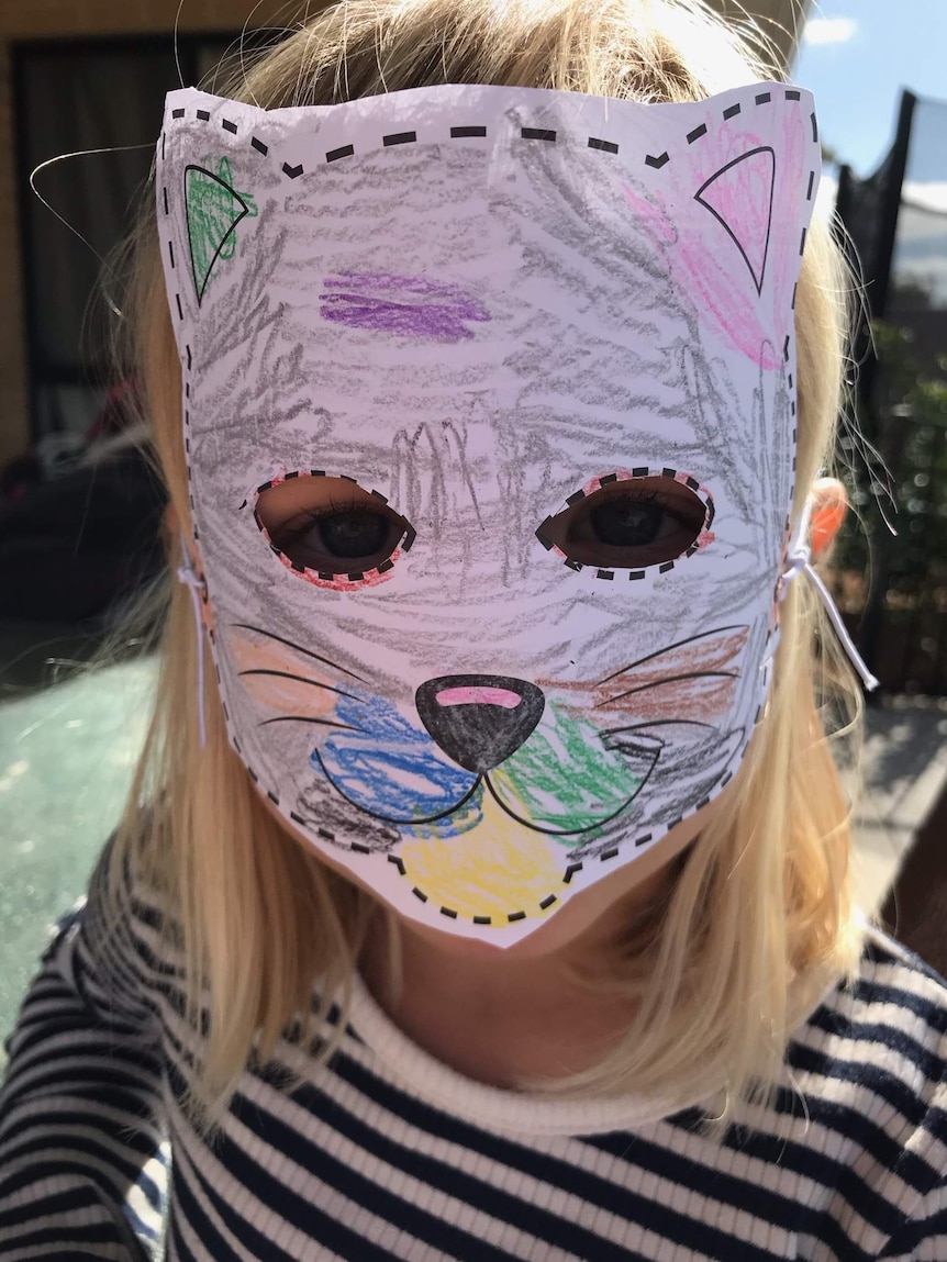 A young girl looks at the camera with a cat mask on.