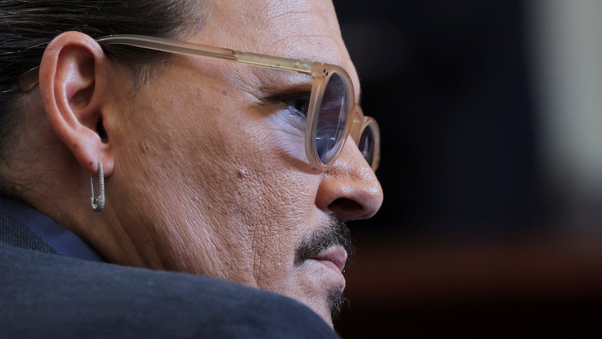 A close shot shows Johnny Depp in profile, wearing pale-rimmed glasses and an earring shaped like a safety pin