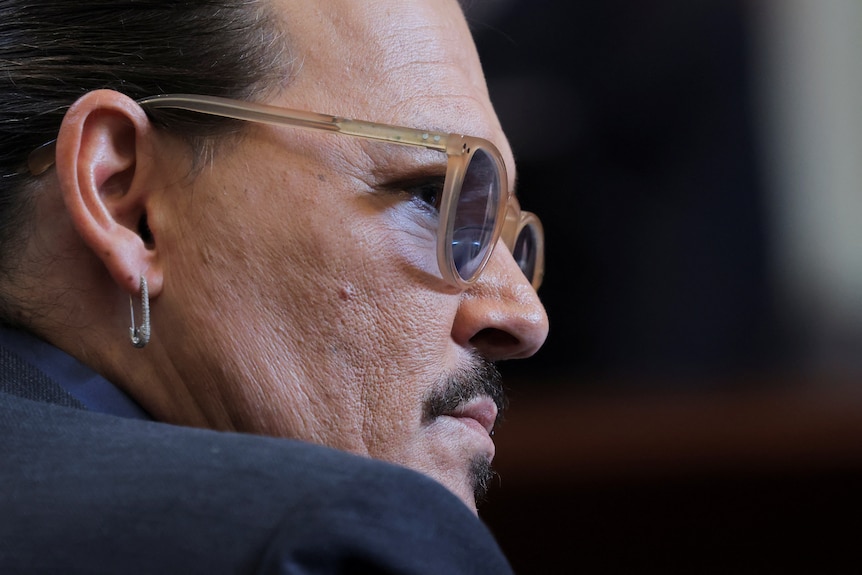 Un primer plano muestra a Johnny Depp de perfil, con anteojos de montura clara y aretes con forma de imperdible.