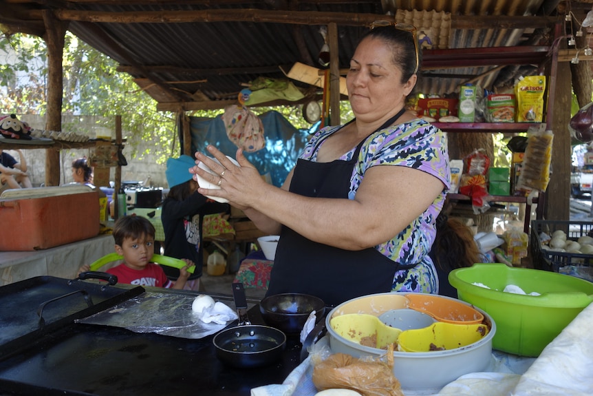 A woman squeezes pastry between her palms with her shop behind her