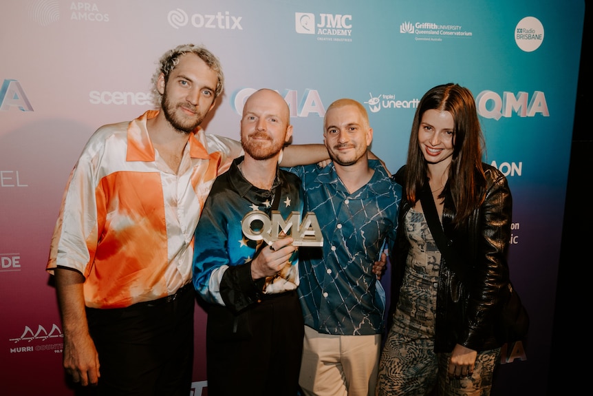 AN image of THe Jungle Giants at the Queensland Music Award ceremony with QMA logo behind them