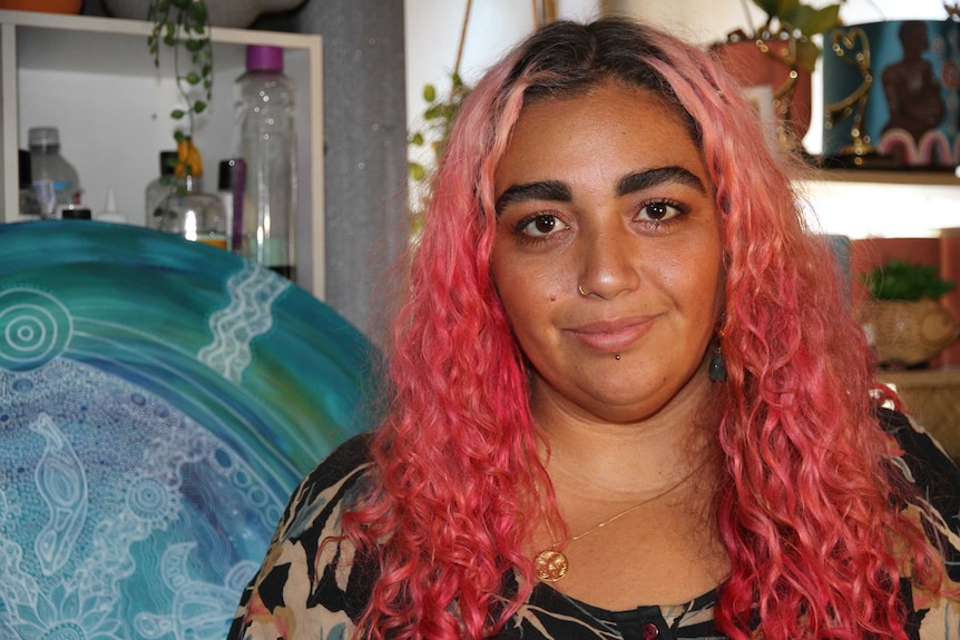 A woman with pink hair stands in front of a blue painting