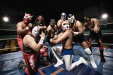 Wrestlers wearing masks stand fiercely in the ring.