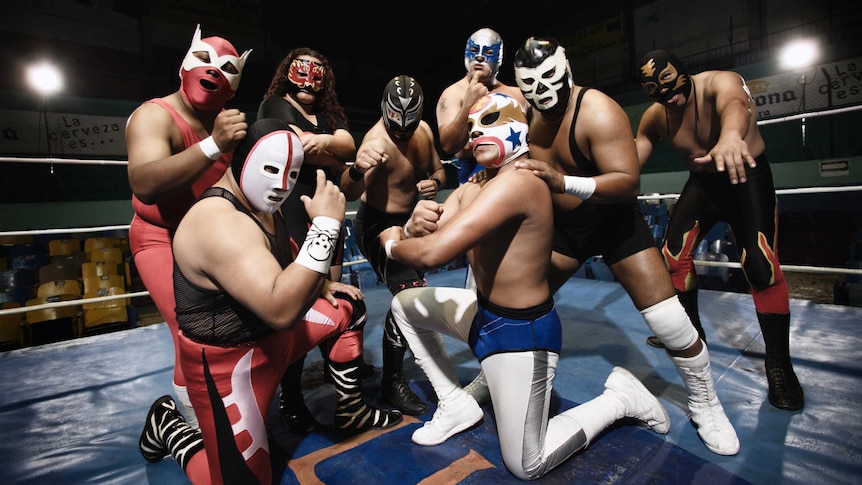 Wrestlers wearing masks stand fiercely in the ring.