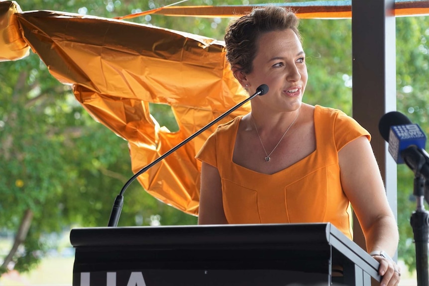 Lia Finocchiaro dressed in orange stands at a lectern at Wharf One on the Darwin Waterfront