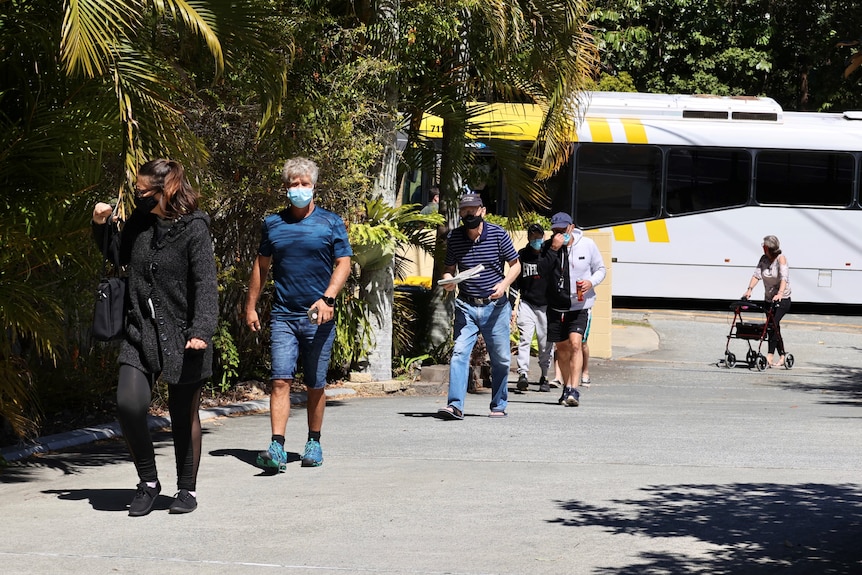 A group of people walking up a drive way from a bus