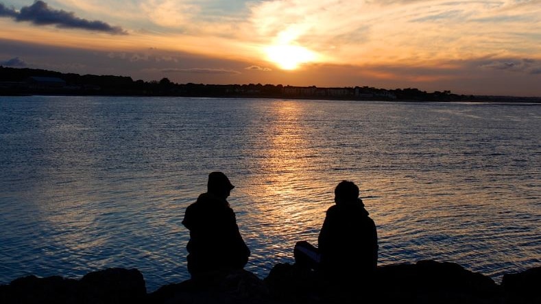 Photo of two people sitting by a lake at sunset 