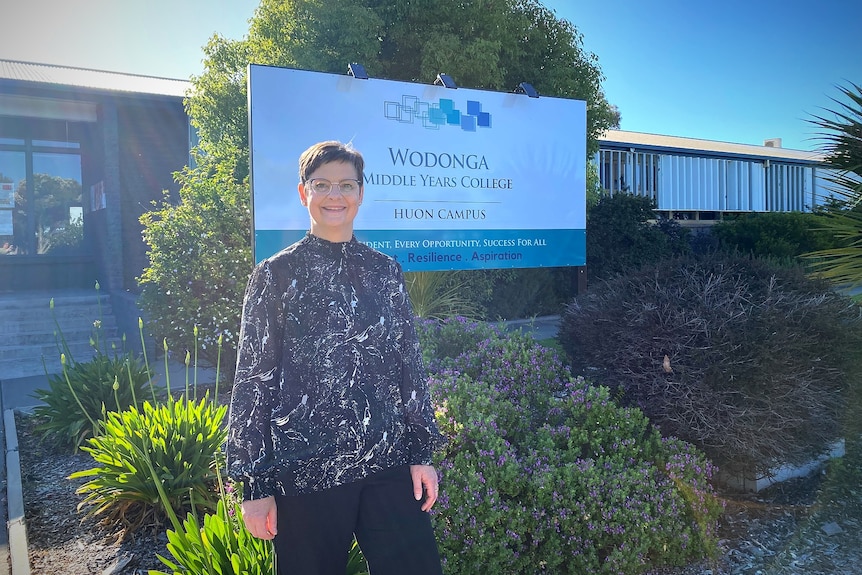 Maree wearing glasses and a dark blouse, standing infront of a Wodonga Middle Years College sign.
