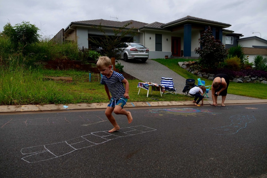 A young boy plays hopscotch on a street.