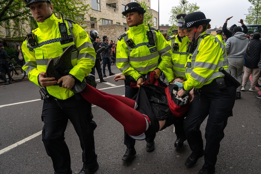  UK Police carry a protester away from blocking a bus taking immigrants to an airport.
