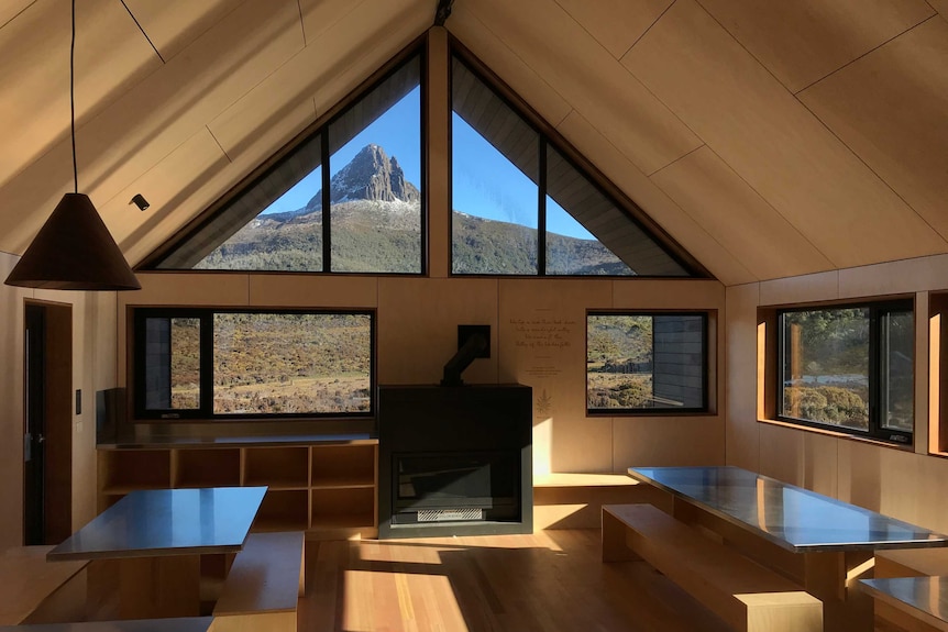 Interior of a hut, showing minimalist design and timber surfaces, with stunning mountain view through window.