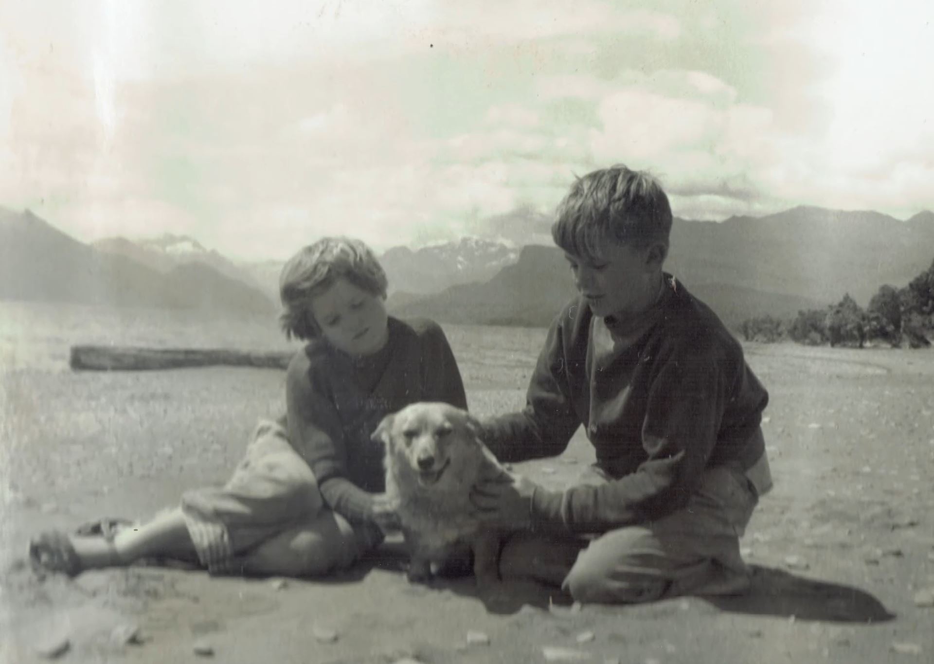 Black and white image young boy and girl sitting on the sand with a dog between them