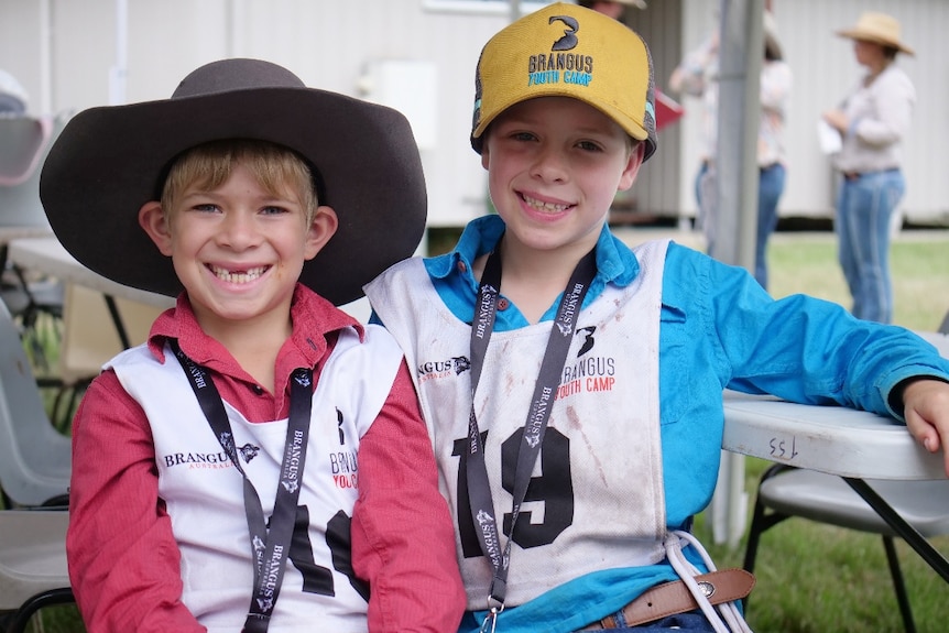 Wilson and Hunter, one in a red shirt and hat, another in a blue shirt and cap smiling, sitting together.