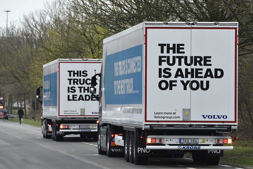 Two self-driving trucks drive together on a highway in Europe.