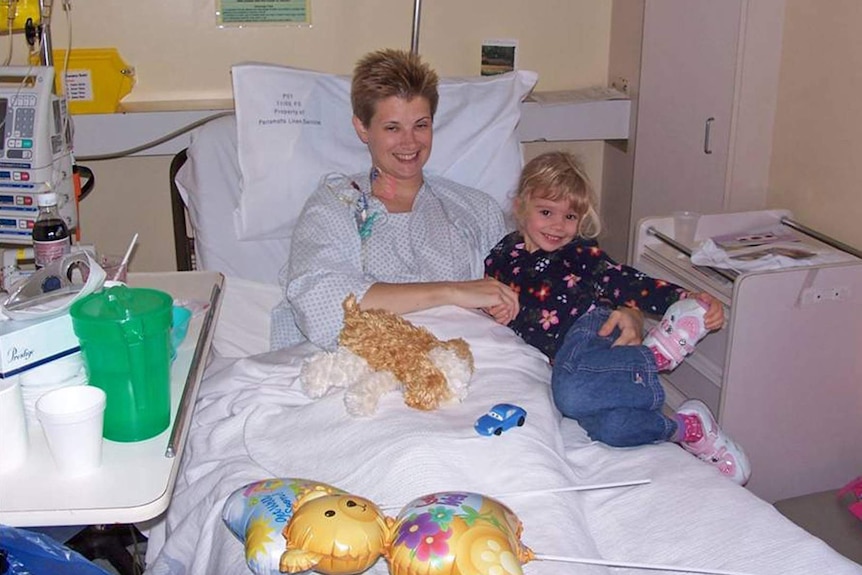 A woman lies in a hospital bed with her young daughter sitting next to her