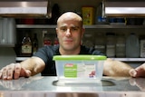 Man standing face on to camera with a plastic food container in a commercial kitchen