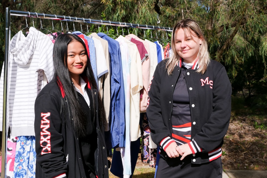 Two teenagers looking at the camera with a rack of clothes behind them