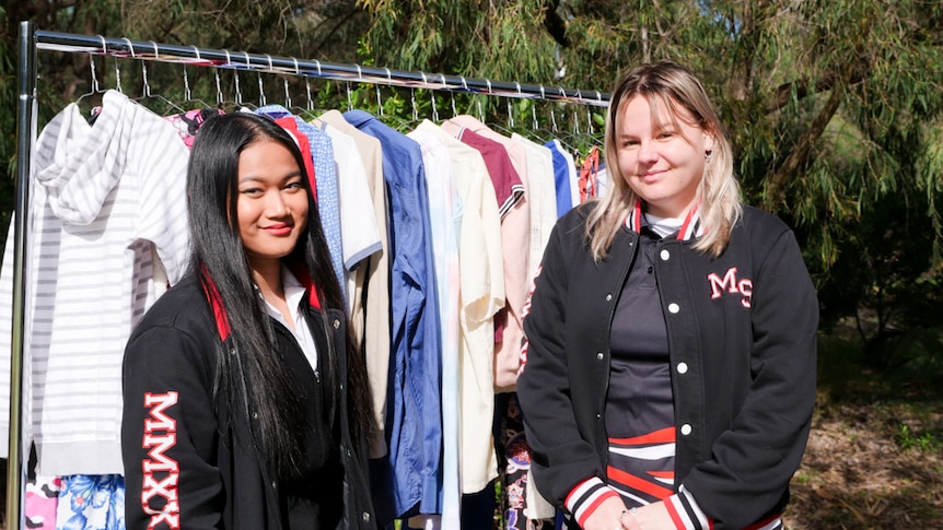 Two teenagers looking at the camera with a rack of clothes behind them