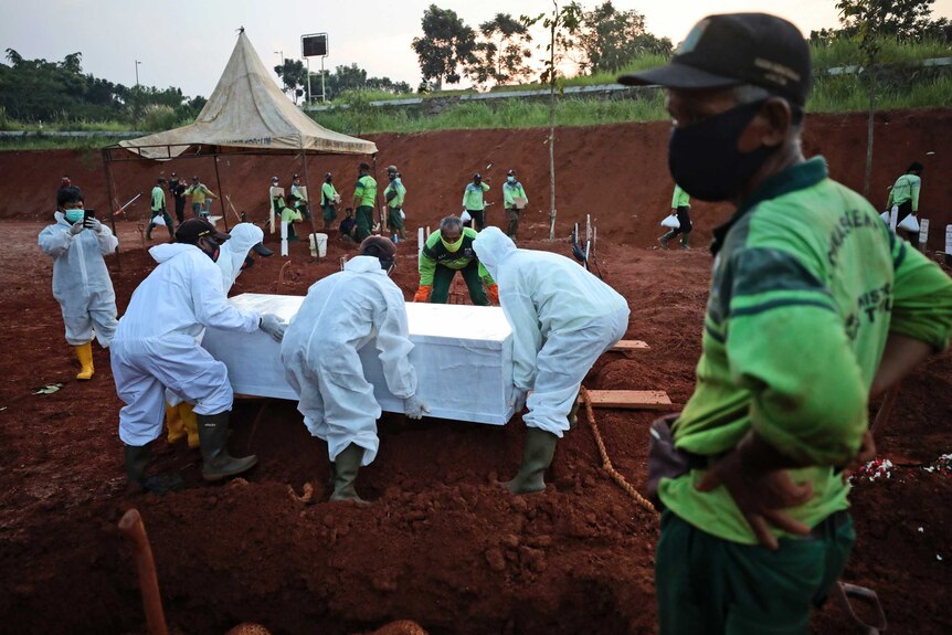Indonesian workers in hazmat suits lower a coffin containing the body of a suspected COVID-19 victim into a grave.