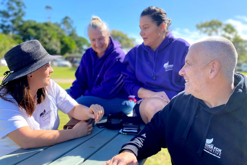 Four people sit around a picnic table smiling and laughing