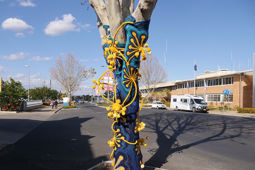 A tree covered in bright blue and gold yarn