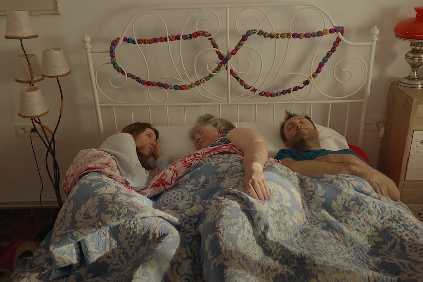 A couple in bed with an older woman lying between them in the web series Cancelled