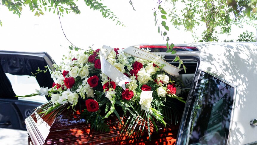 A casket with red roses on top in the back of a hearse.