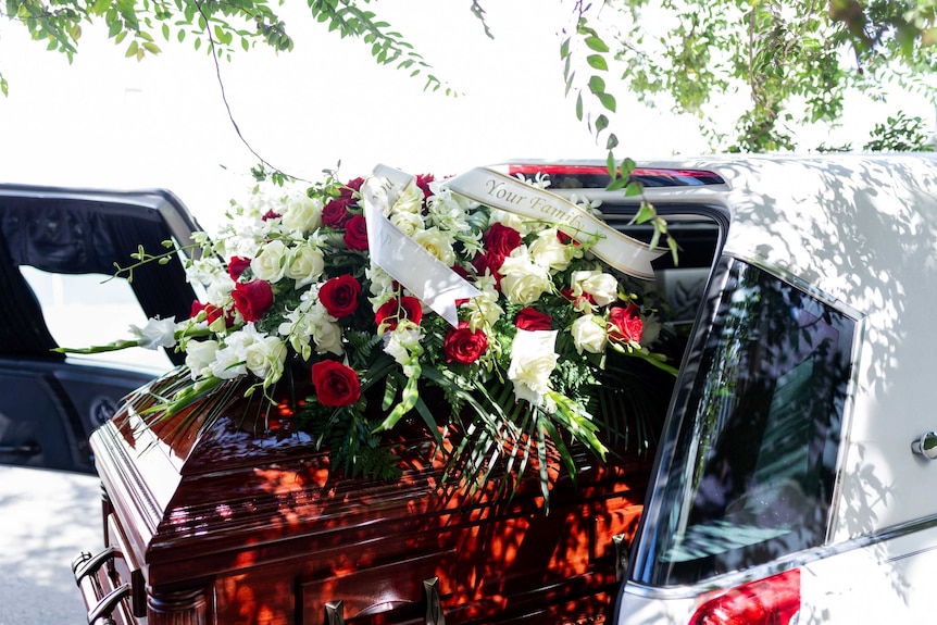 A casket with red roses on top in the back of a hearse.