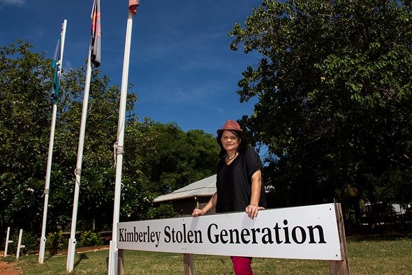 Tania Bin Baker stands outside the Kimberley Stolen Generation Aboriginal Corporation building, resting her hands on the sign.