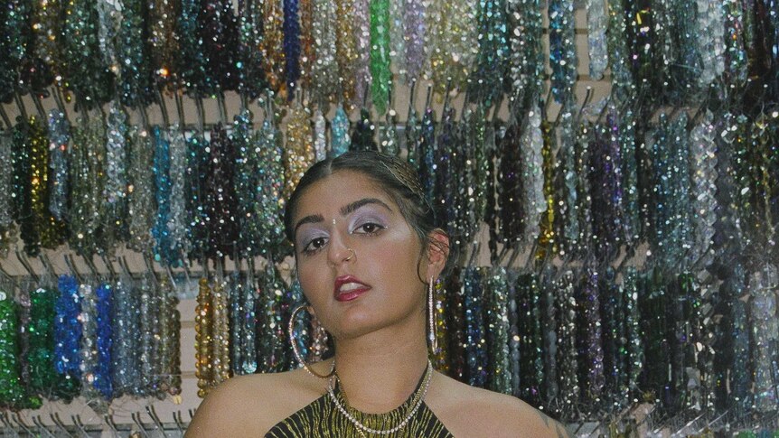 Chippy Nonstop wearing a 'glam' halter neck top standing in front of a wall of sparkling necklaces.