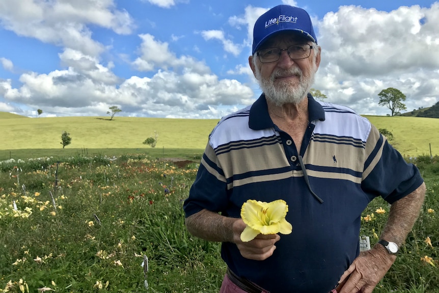 Scott Alexander looks at the camera with a flower in his hand and daylilies behind him.