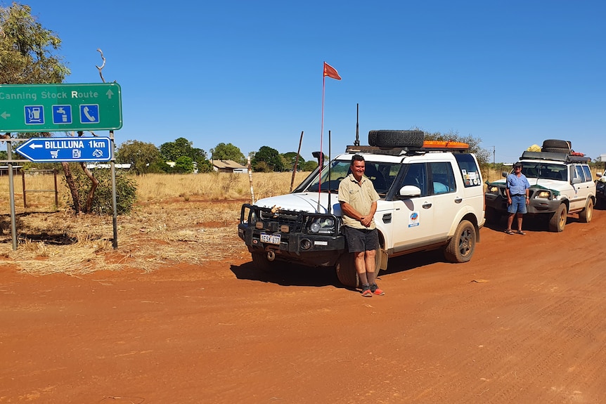 Three white cars line up on side up red dirt track. Sign indicates direction of Billiluna and direction of Canning Stock Route