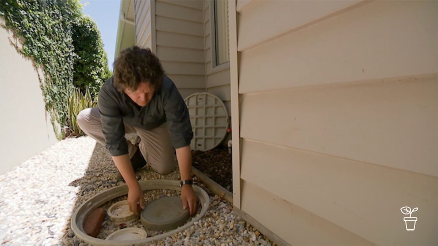 Man crouching on ground looking at underground pipes in garden