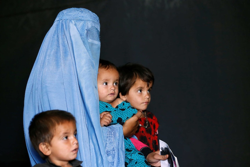 A women covered by a blue burka stands with three children.