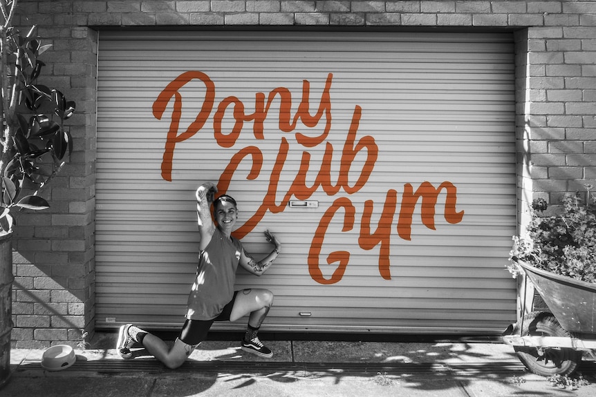 A woman kneels in front of the Pony Club Gym garage.
