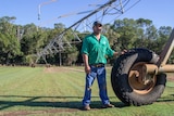 a man leaning on the wheel of a centre-pivot with grass underneath.