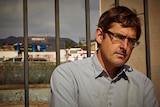 Louis Theroux standing in front of a fence