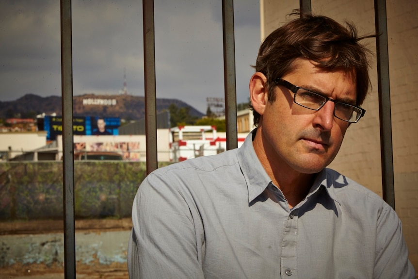 Louis Theroux standing in front of a fence