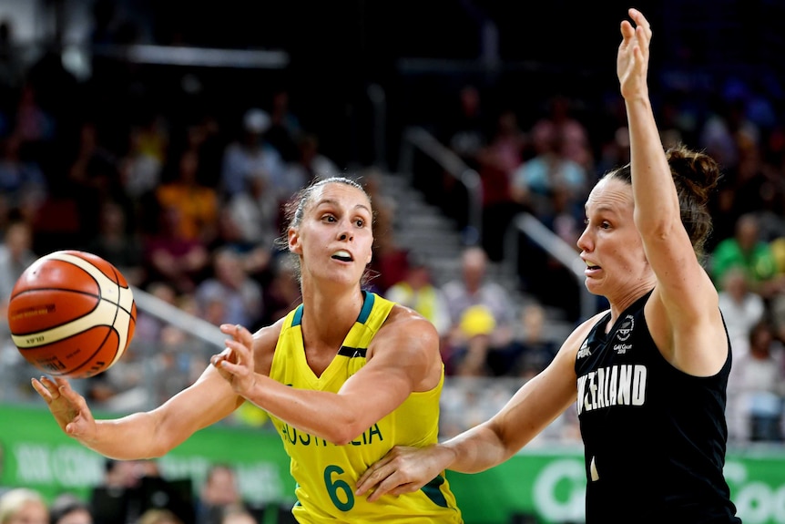An Australian Opals player holds the basketball as a New Zealand opponent defends.