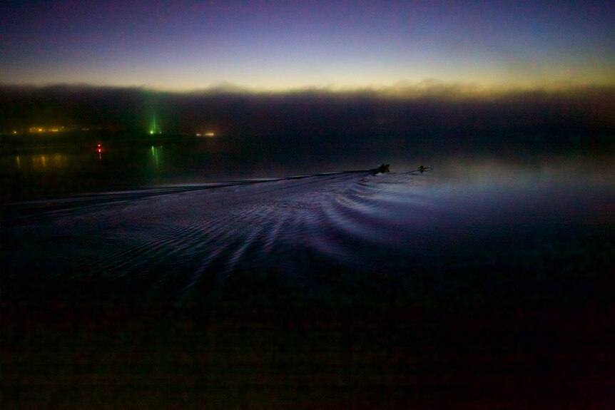 The first rower of the morning breaks the mirror-like surface of Lake Burley Griffin