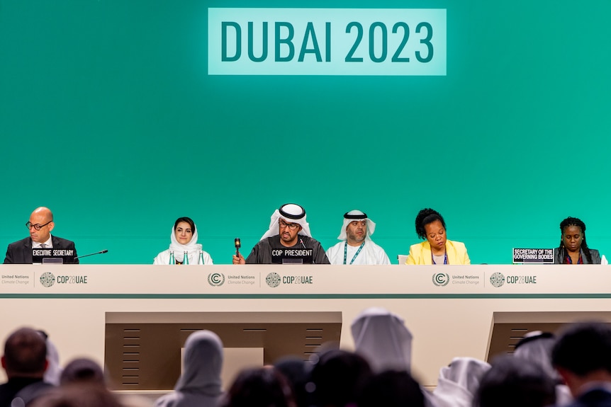 The COP28 president sits on a panel on stage, speaking into a microphone, three women and two men on stage with him.