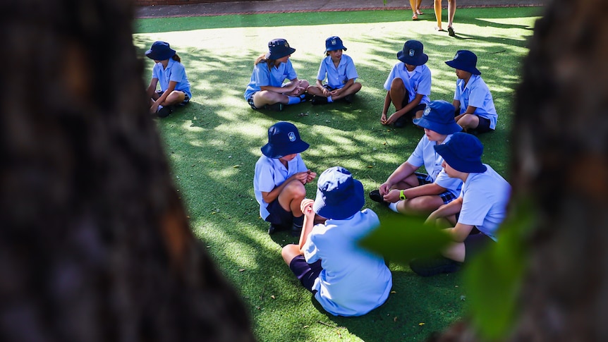 Young school children sitting outdoors in the playground.