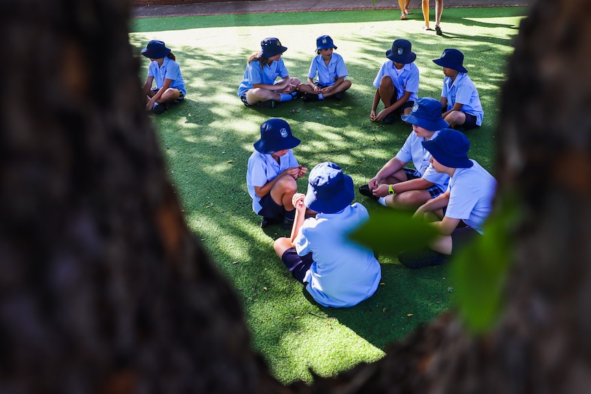 students wearing hats sitting on the grass at school